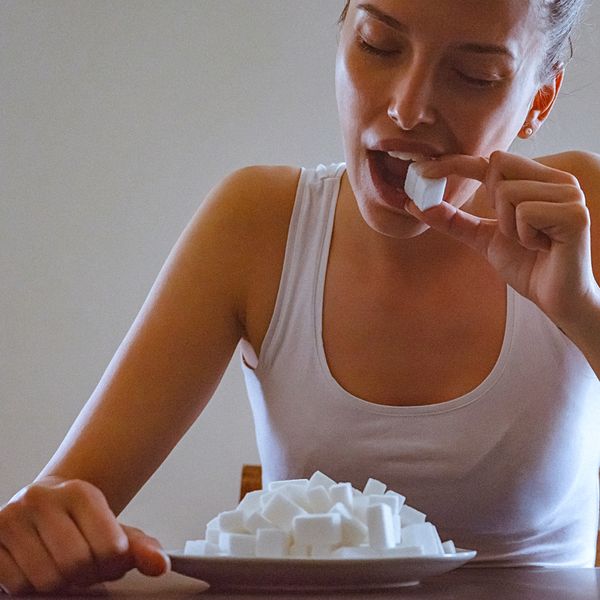 Close-up of a young woman eating sugar cubes. There is a plate full of sugar cubes, on the table before her.