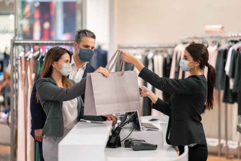 Couple shopping at clothing store and retail worker helping