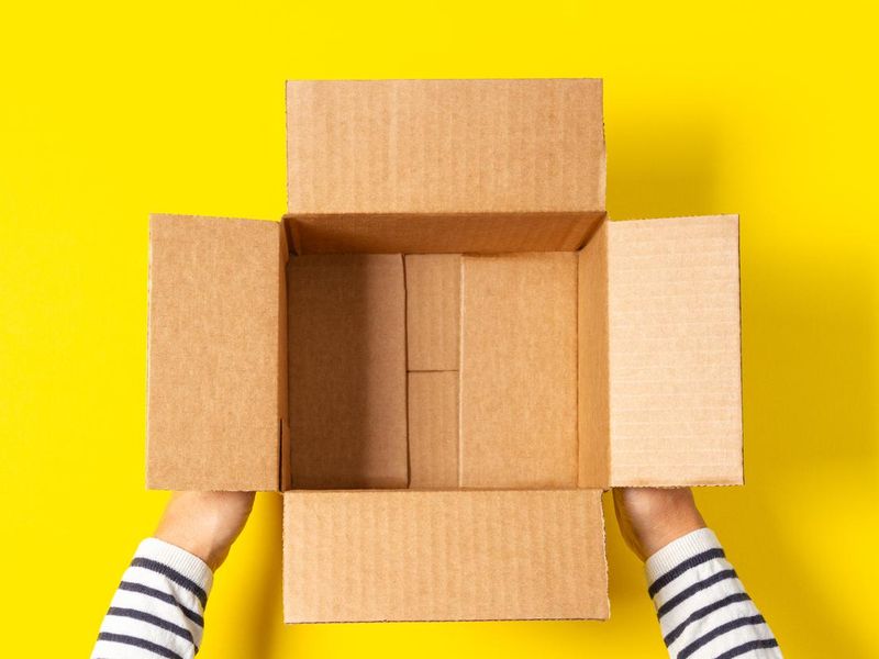 Female hands with empty open cardboard boxes on yellow background. Top view