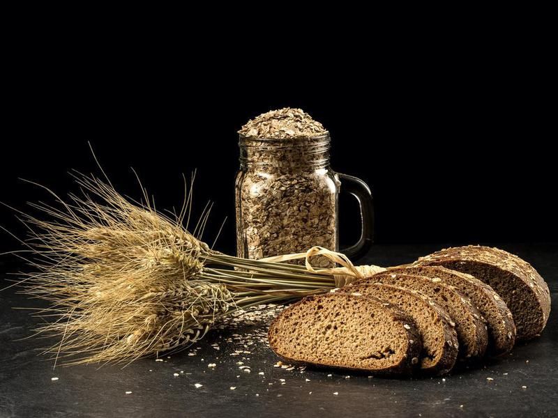 Grain bouquet, golden oats spikelets in jar on dark wooden table, buns and can filled with dried grains.