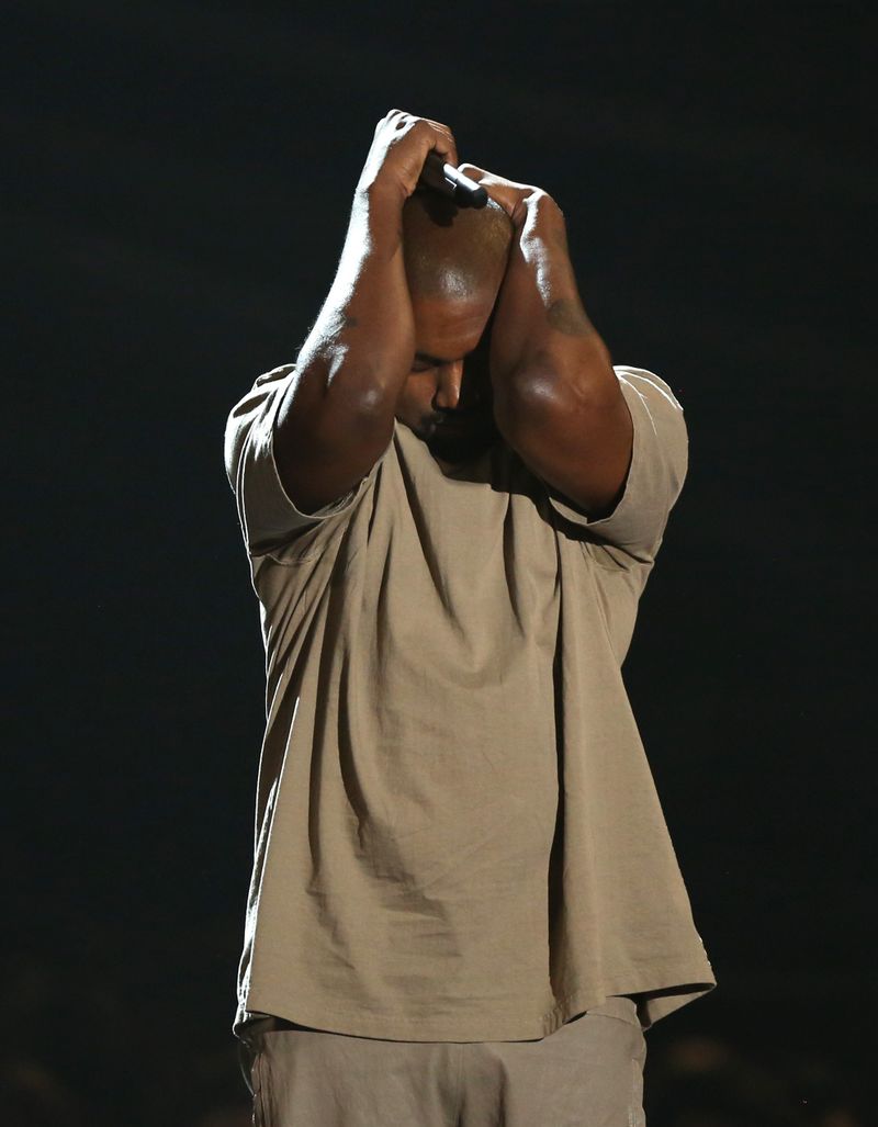 Kanye West with his hands on his head on stage