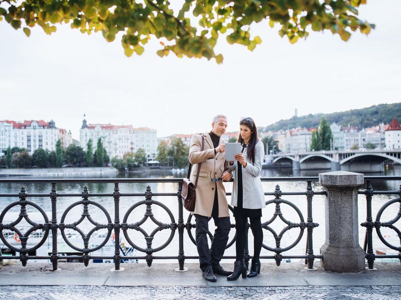 Man and woman business partners with tablet standing by a river in Prague