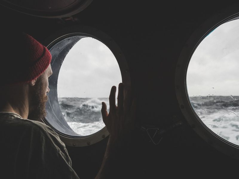 Man at the porthole window of a vessel in a rough sea