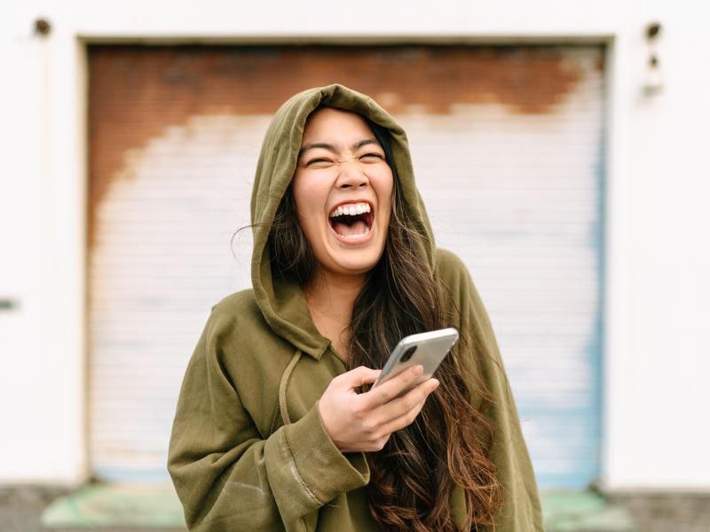 Portrait of young woman holding smart phone and laughing
