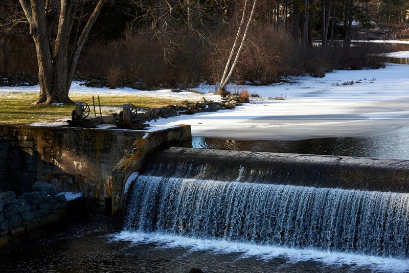 Water flows over a small dam that creates an old mill pond on the Oyster River in Durham, NH.