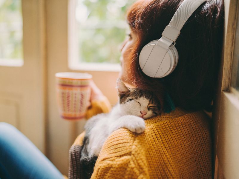 Woman at home listening to music and drinking coffee with kitten