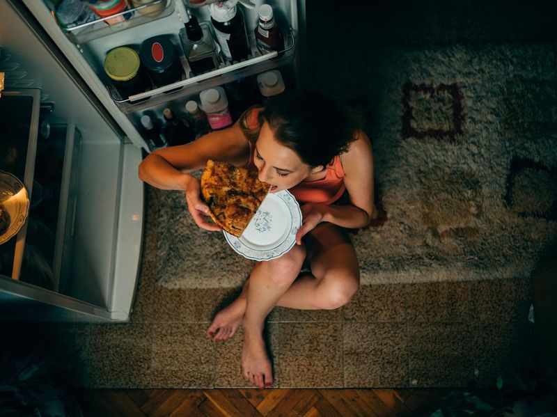 Woman eating in front of the refrigerator in the kitchen