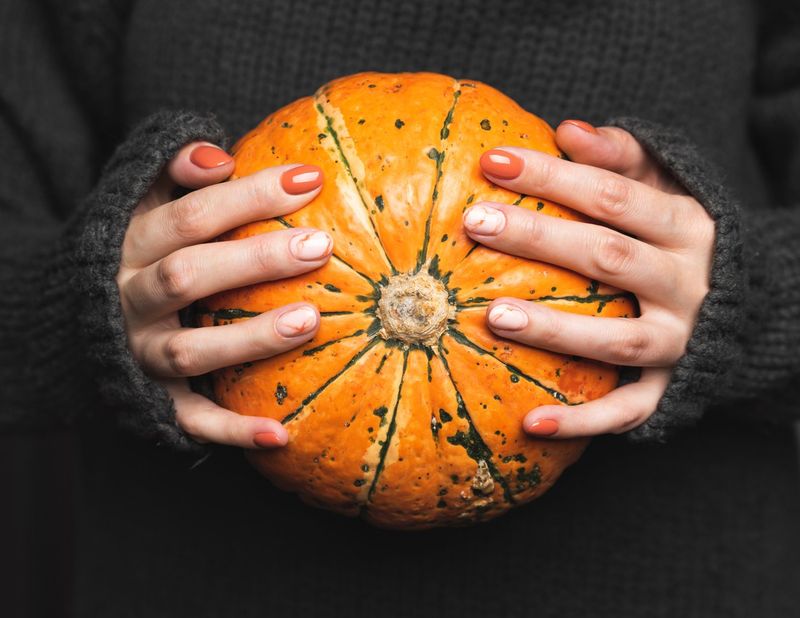 Woman in a grey knitted sweater holds a pumpkin.