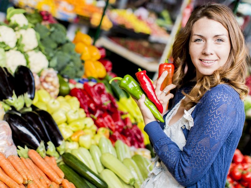 Young woman shopping for vegetables and holding peppers